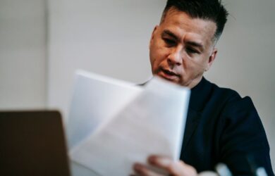 Yrittäjä tarkastelee asiakirjoja kannettavan tietokoneen ääressä