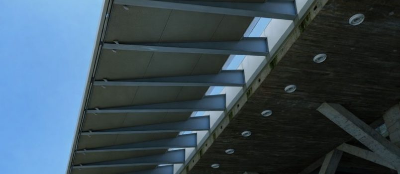 Modernin rakennuksen julkisivun yksityiskohta metallirakenteista ja betonista sinistä taivasta vasten.